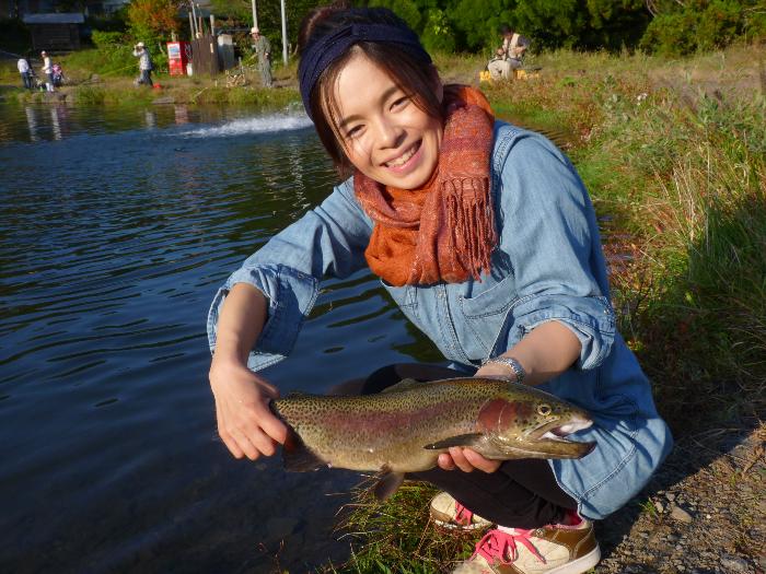 川岸で釣った魚を手に持ち笑顔を見せる女性の写真